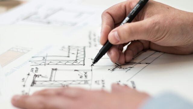Close-up of hand drawing intricate technical designs on blueprint with pen, ideal for engineering or architecture themes.