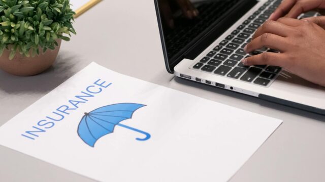Close-up of hands typing on laptop with an insurance document visible on the desk.